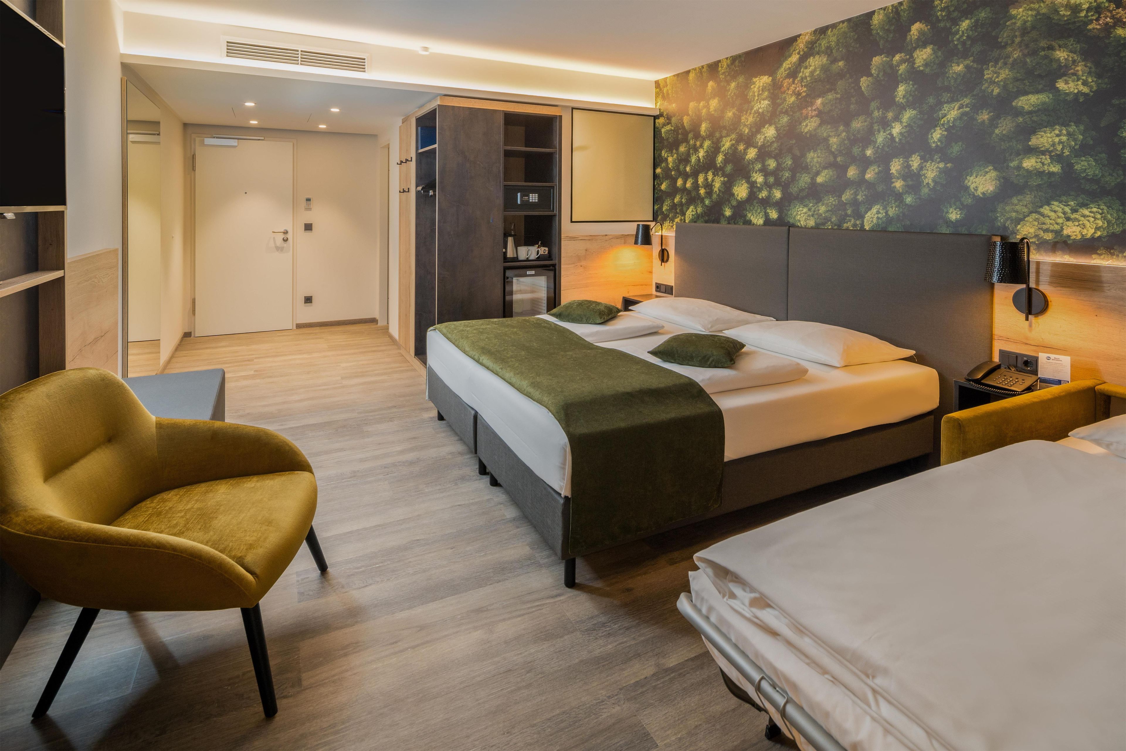 A hotel room with a bed, a chair, a desk, a wardrobe, and a wall-mounted TV.