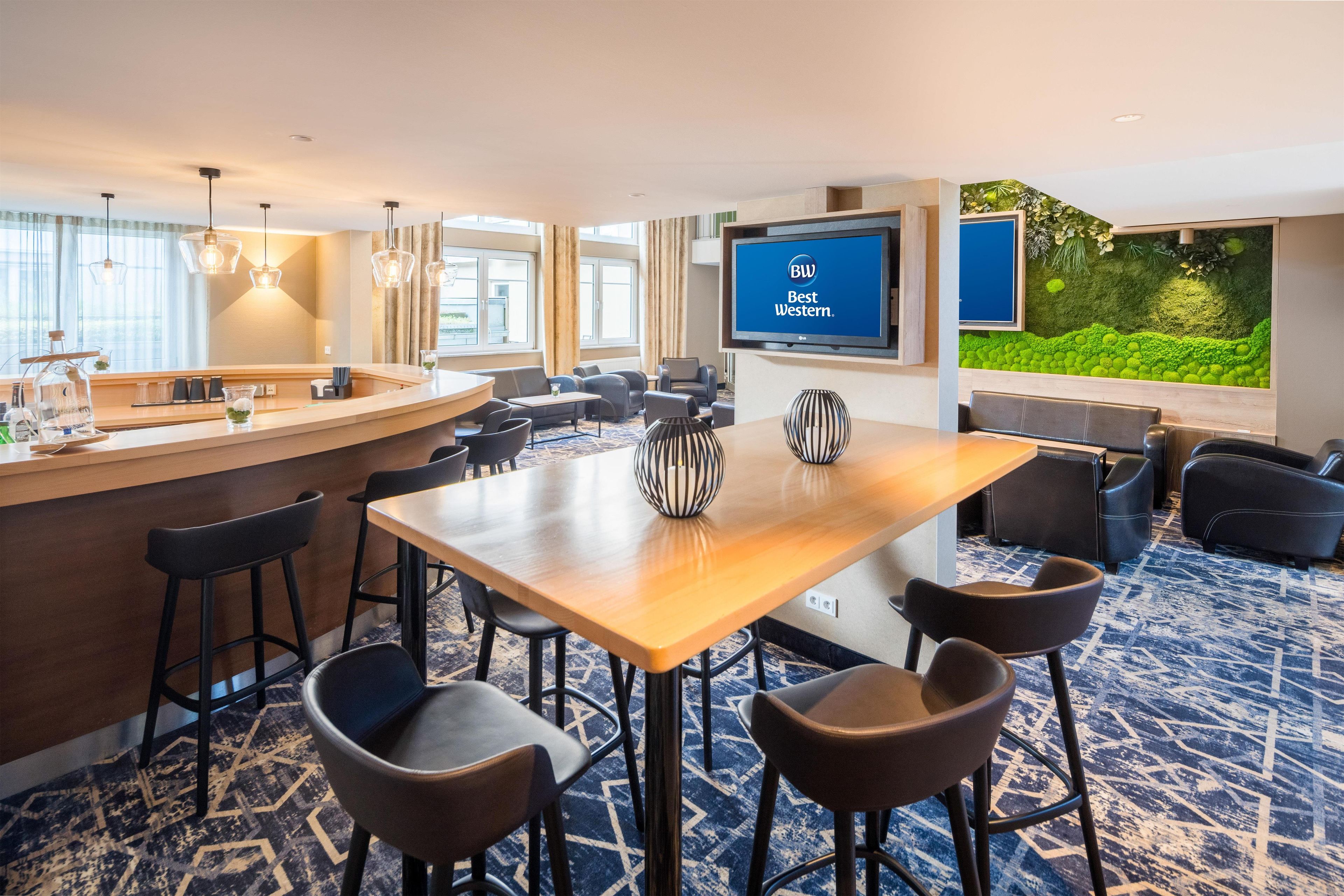 A hotel lobby with a reception desk, bar area, seating arrangements, and a large screen displaying 'BW Best Western.'
