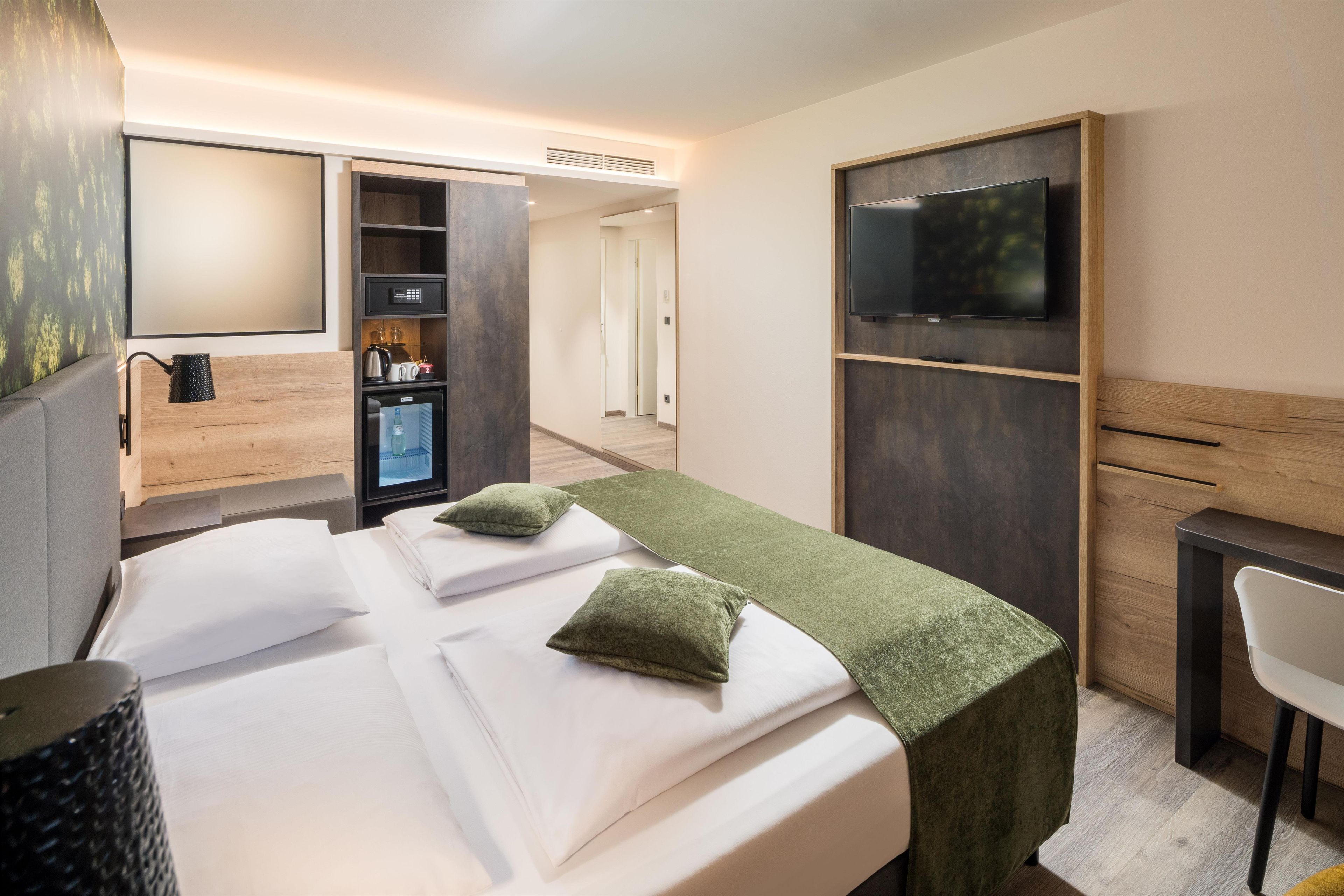 A hotel room with a bed, a TV, a desk, and a minibar.
