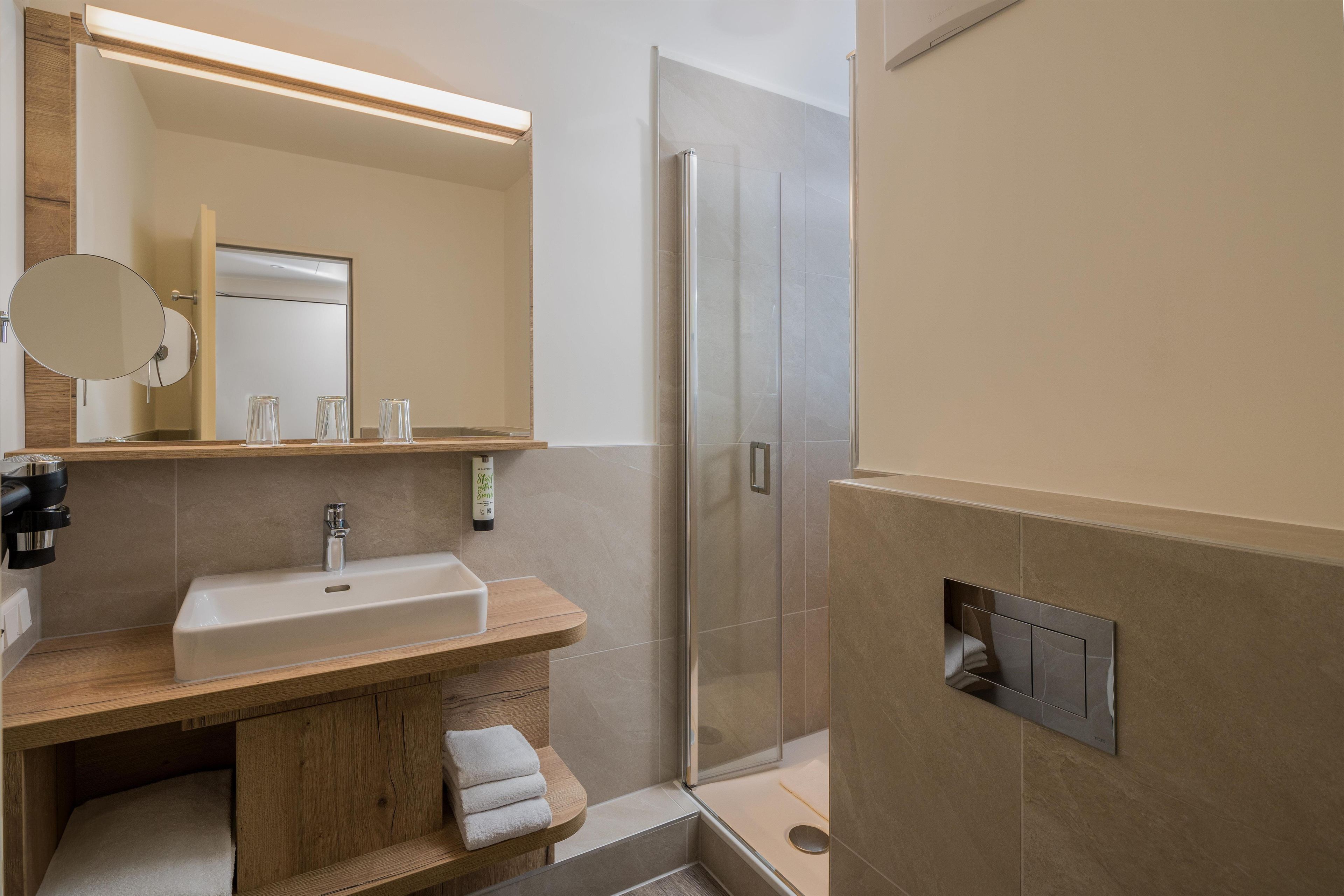 Un baño moderno con lavamanos, espejo, toallero y zona de ducha.