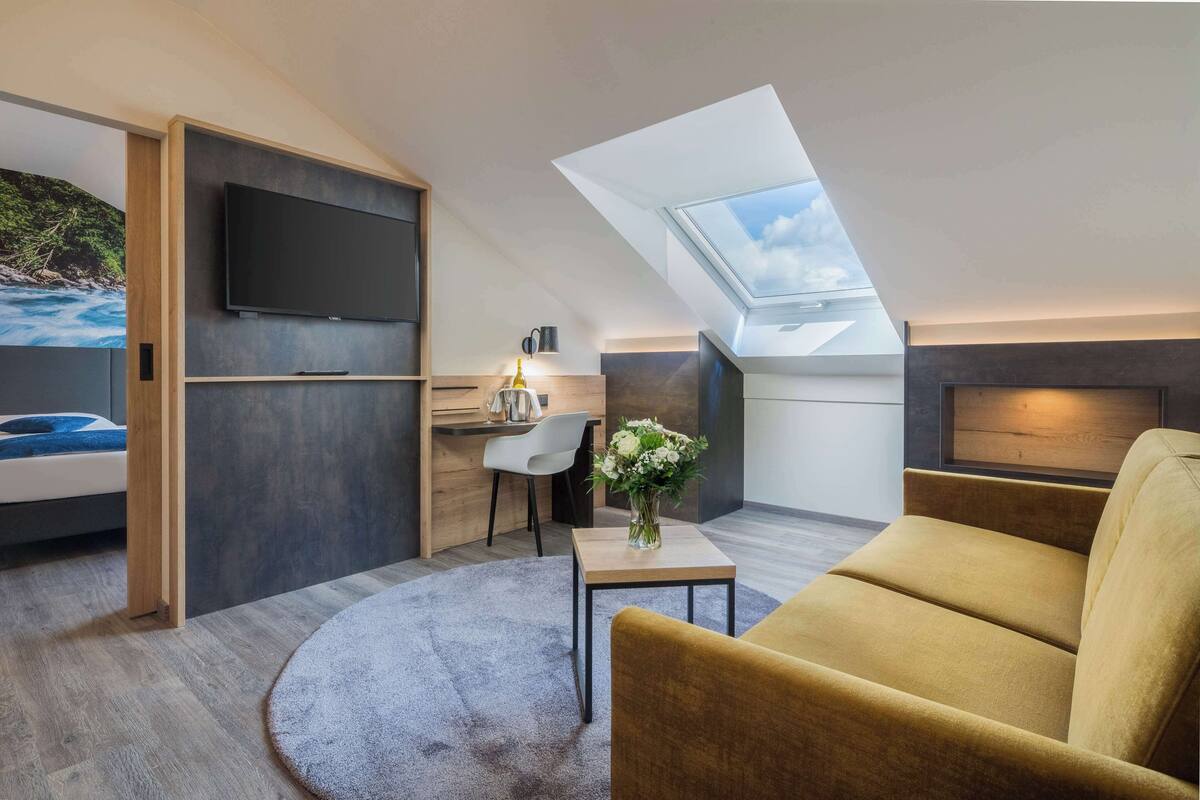 Een moderne loft slaapkamer met dakraam, een flatscreen televisie, bureau en een comfortabele zithoek.