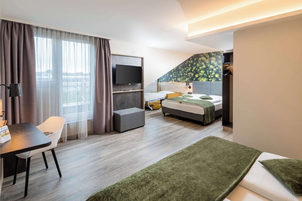 Een moderne hotelkamer met een bed, een bureau, een stoel, een televisie en een groot raam met gordijnen.