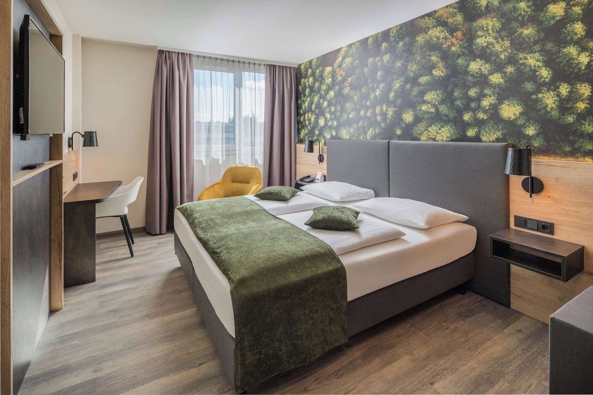 Een moderne hotelkamer met een bed, een bureau, een stoel, een televisie en een muur met een natuurdecoratie.