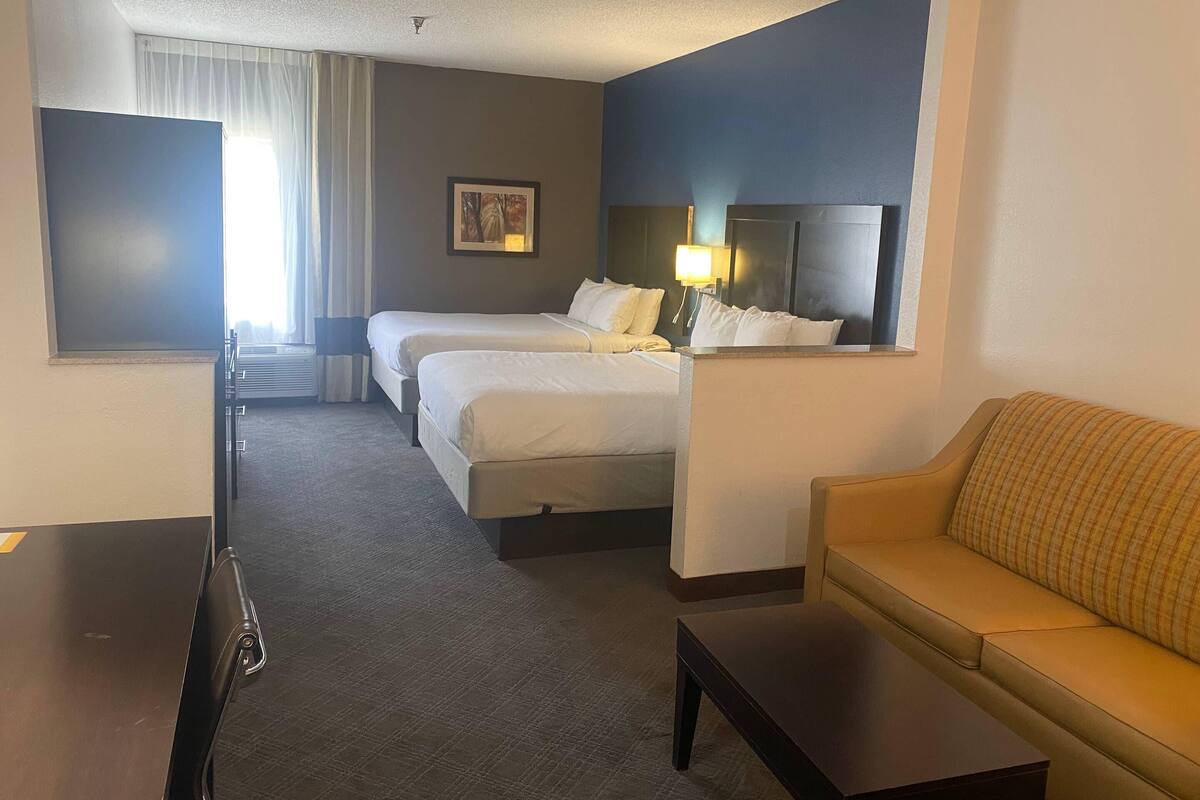 Ein Hotelzimmer mit zwei Betten, einem Schlafsofa, einem kleinen Tisch und einem Fernseher.