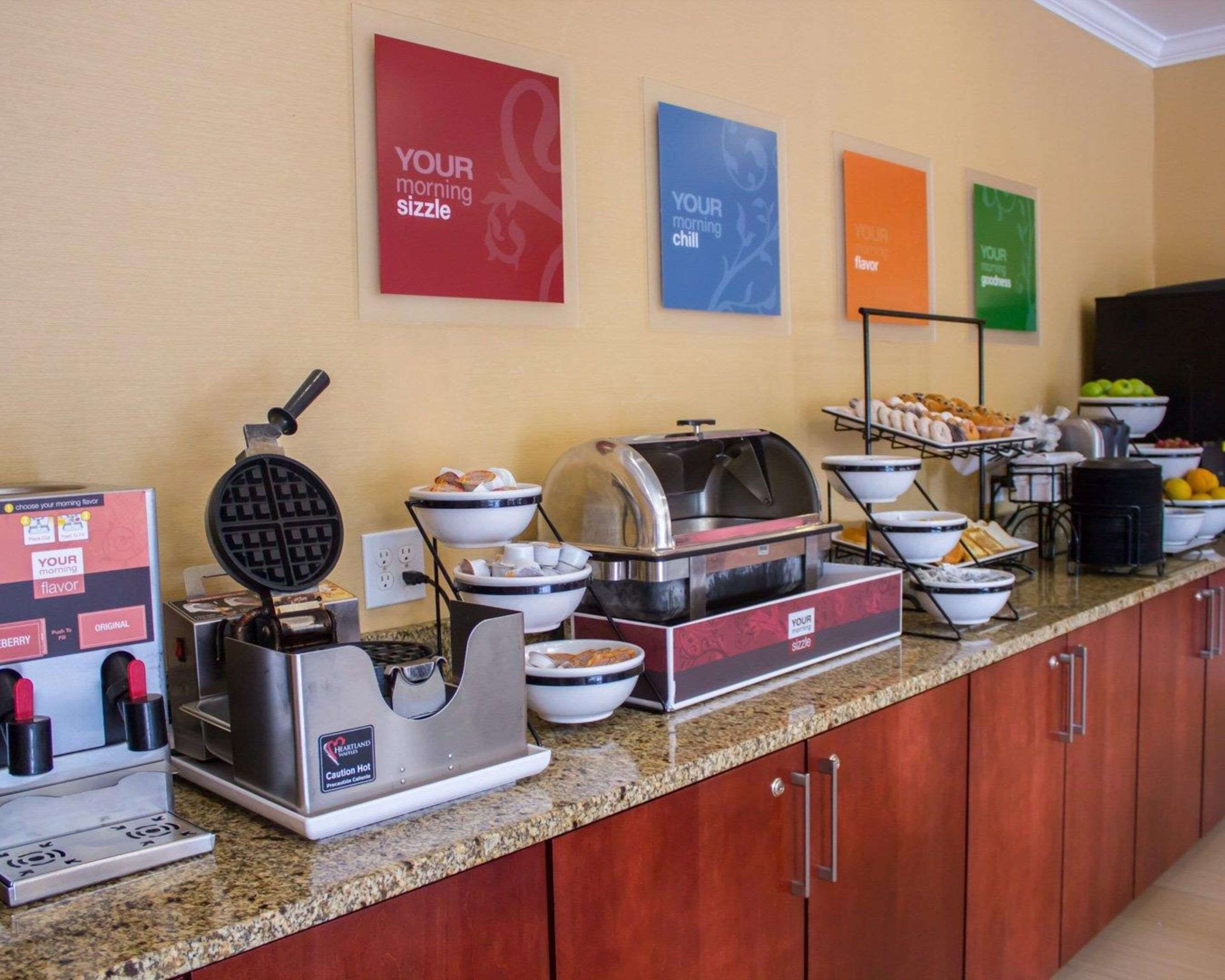 A breakfast buffet with waffle irons, bowls of food, and a coffee maker.