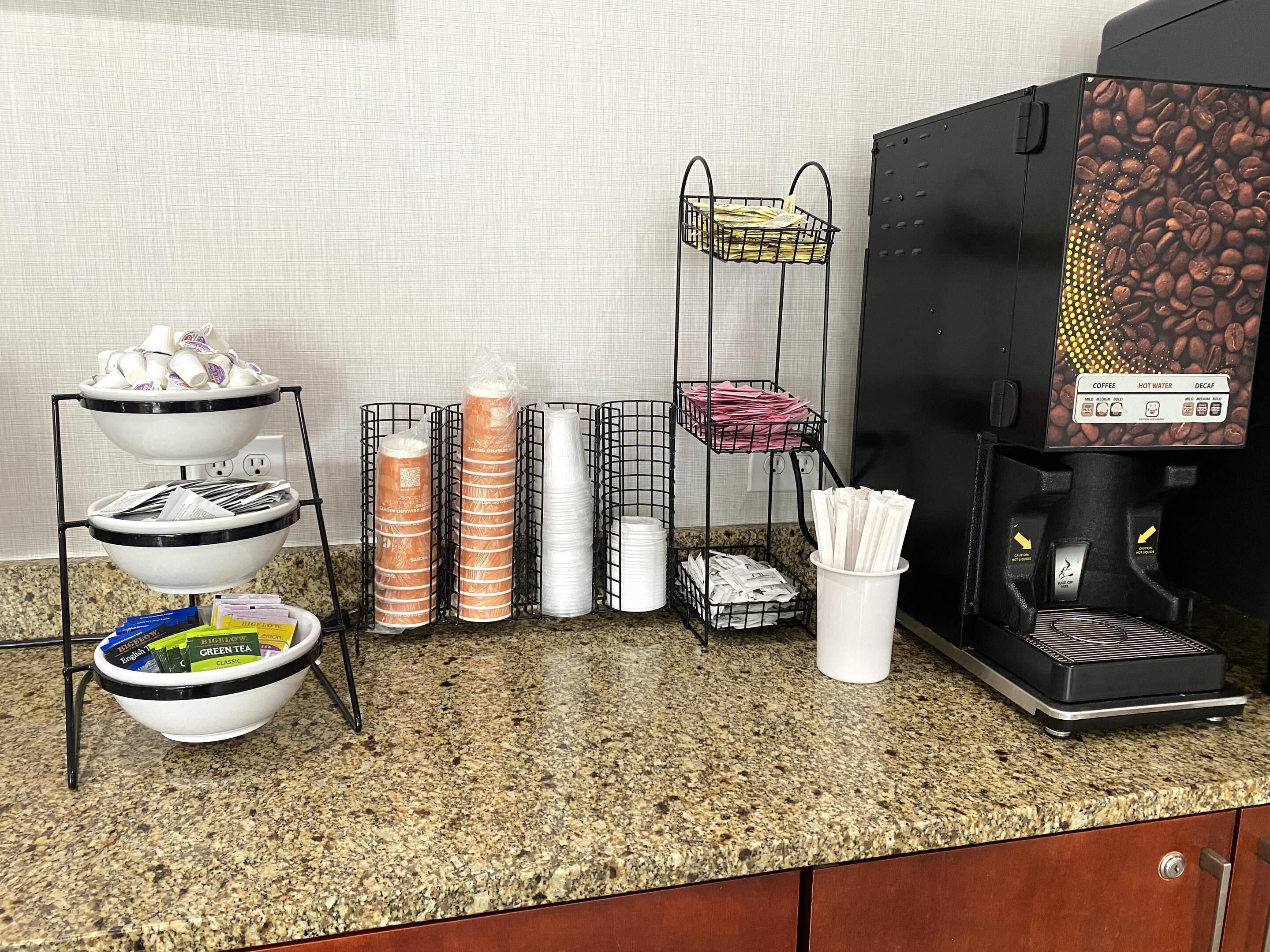 A coffee station with a coffee machine, paper cups, and a tray of disposable cups.