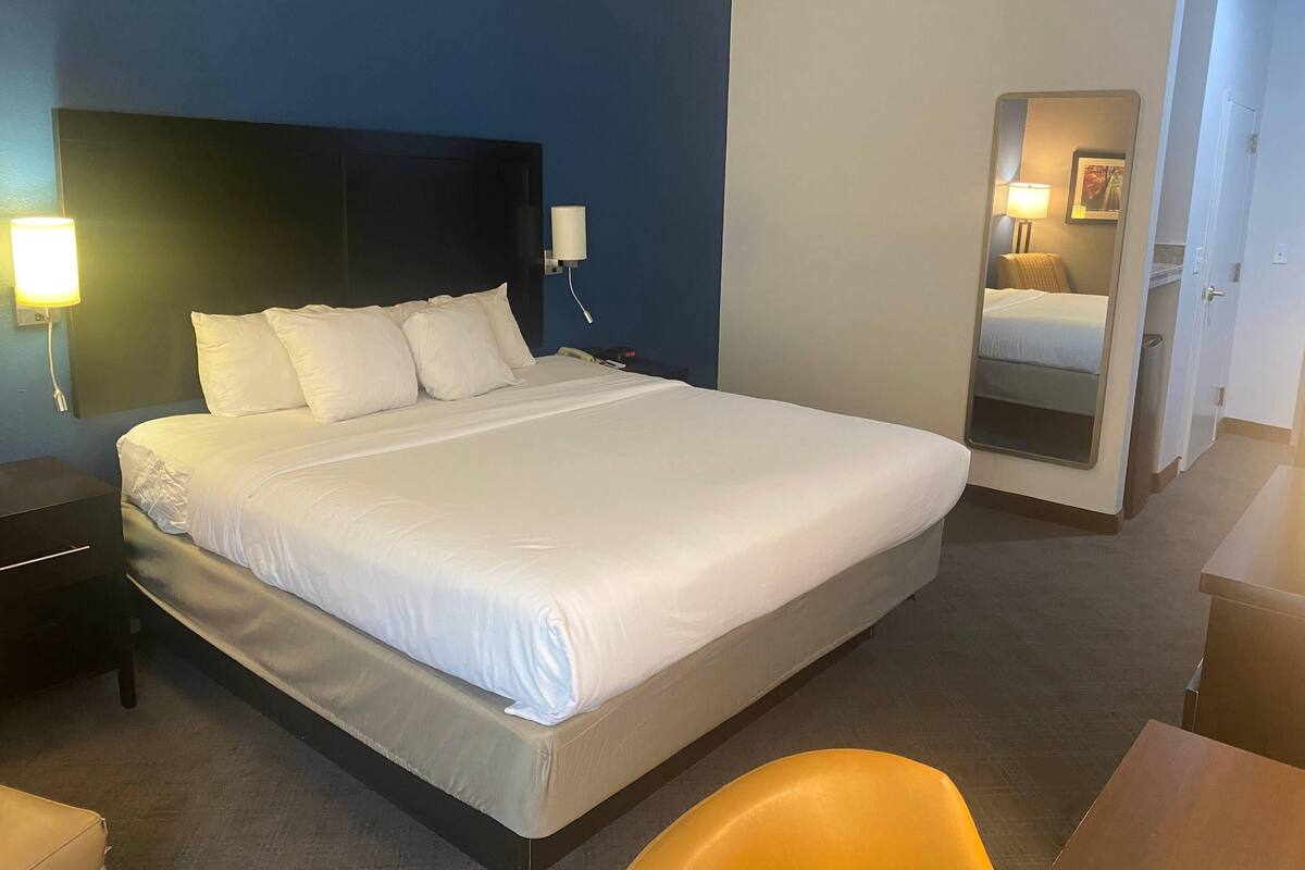 Ein Hotelzimmer mit einem großen Bett, Nachttischlampen, einem Telefon am Nachttisch und einem Spiegel an der Wand.