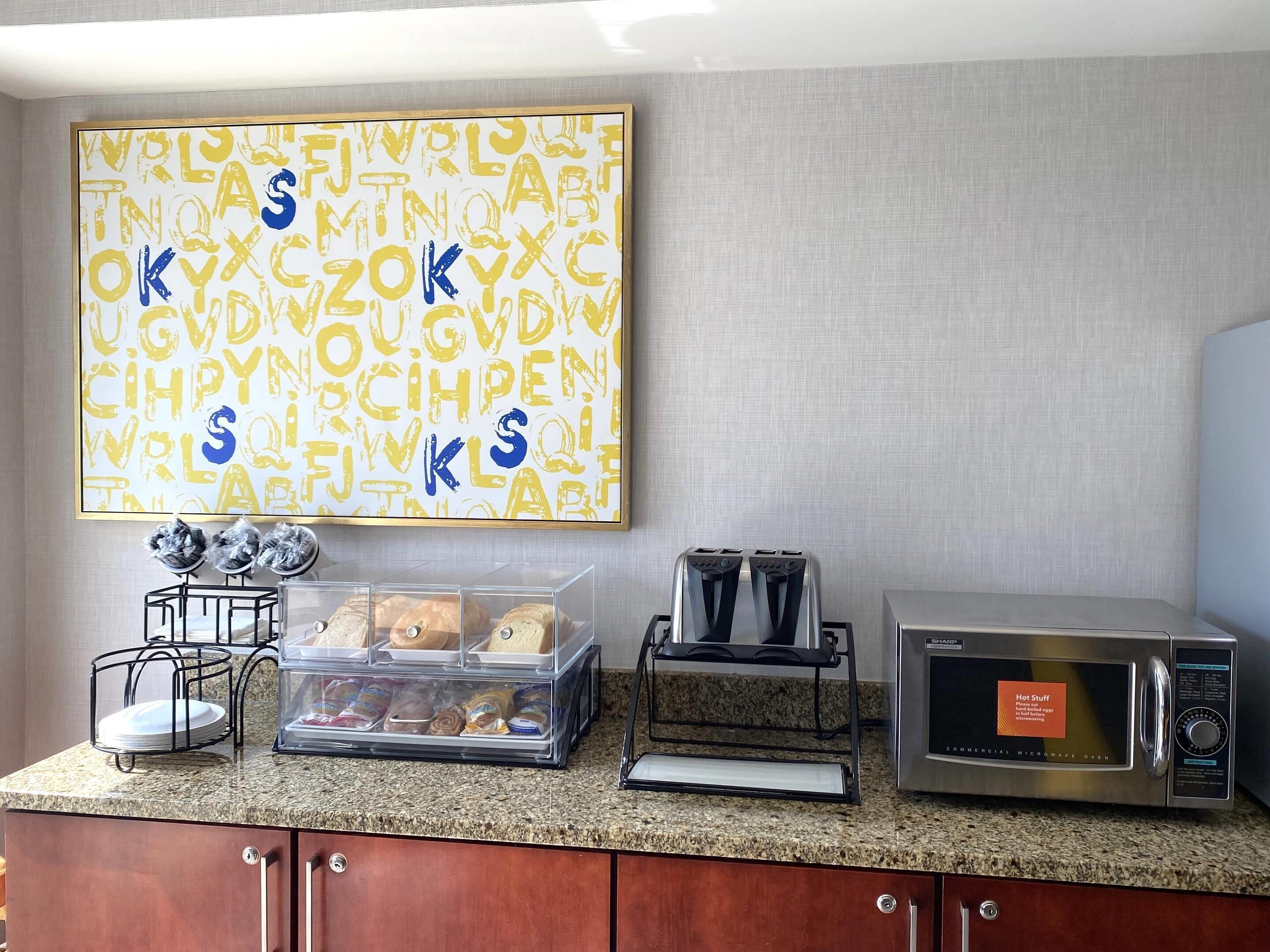 A kitchen with a granite countertop, a toaster, a microwave, a bread bin, and a decorative wall art piece.