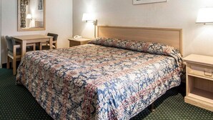 Une chambre d’hôtel avec un lit, un bureau, une chaise, une table de chevet, une lampe, un miroir et un tableau encadré au mur.