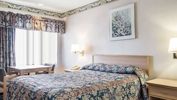 A hotel room with a large bed, a desk, a chair, and a nightstand.