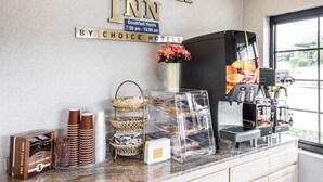 Dans le Rodeway Inn, un coin petit-déjeuner est aménagé avec une machine à café, des paniers de viennoiseries et un panneau indiquant les heures du petit-déjeuner.