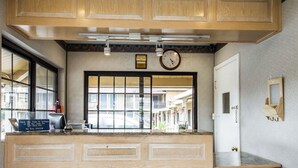 Une cuisine avec des meubles de rangement en bois, une horloge et une fenêtre donnant sur un quartier résidentiel.
