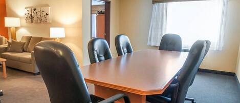 A conference room with a wooden table and six black chairs. There is a sofa and a lamp in the adjacent living area.