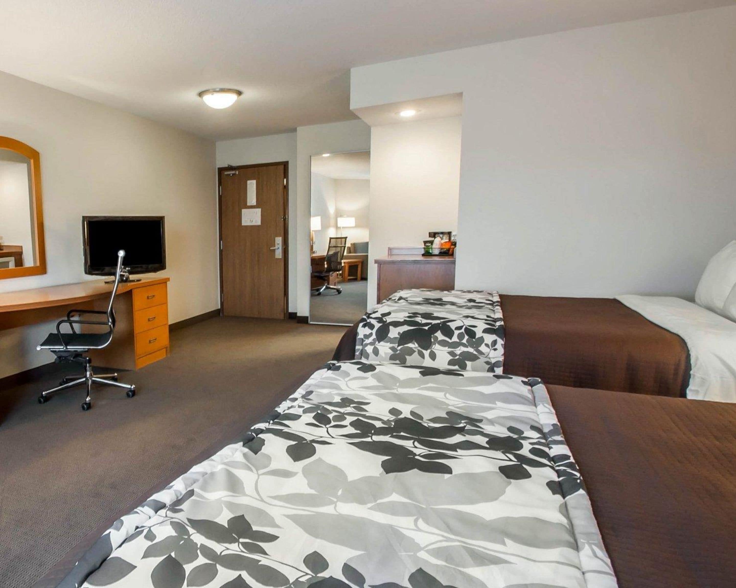 Quarto de hotel com duas camas, uma escrivaninha com cadeira, televisão e porta para o banheiro.