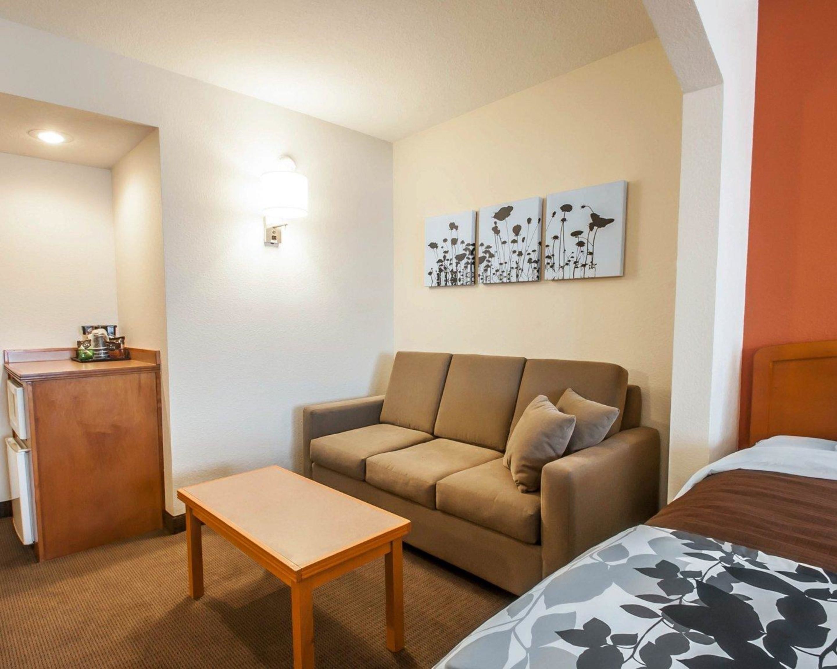 A hotel room with a sofa, a small wooden table, a bed with a floral bedspread, and three wall-mounted artworks depicting flowers.