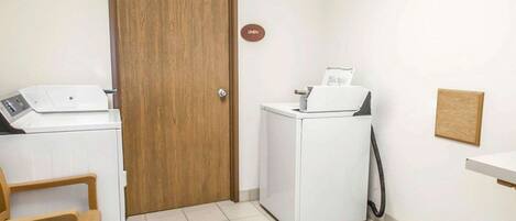 A laundry room with a wooden door, a white washing machine, a dryer, and a small wooden chair.