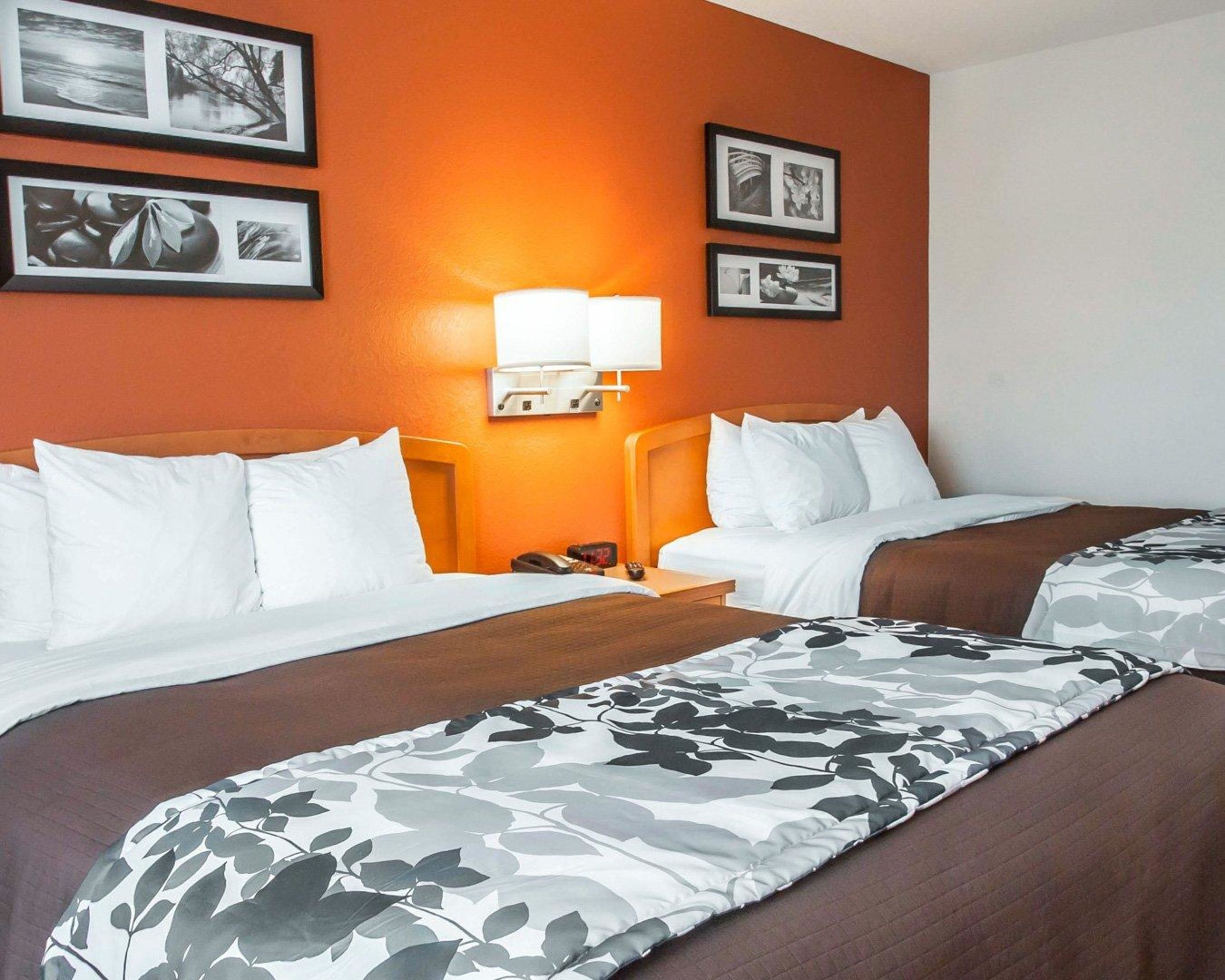 A hotel room with two beds, a nightstand, a lamp, and three framed pictures on the wall.