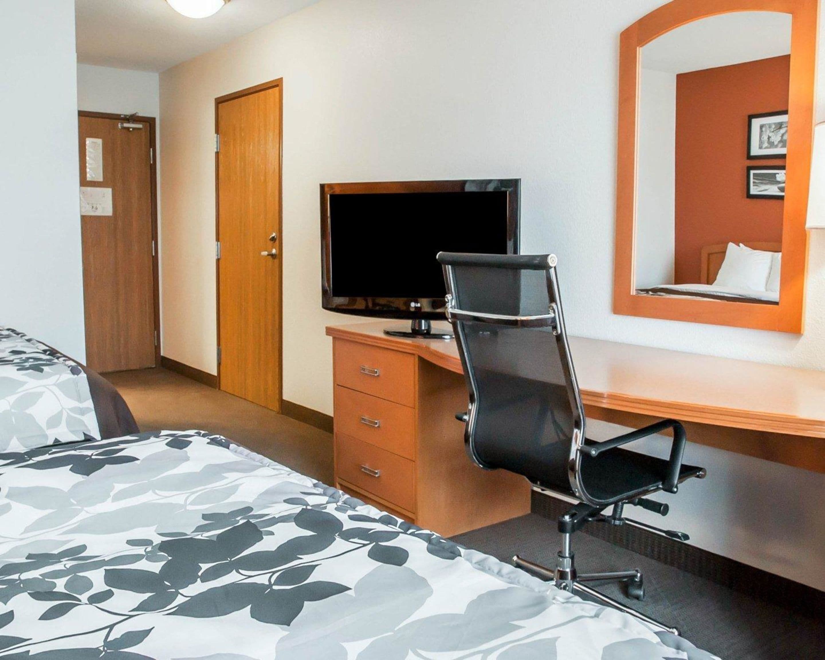 A hotel room with a bed, a desk with a computer, a chair, and a TV.