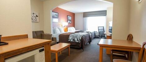 A hotel room with a bed, a desk, a chair, a microwave, and a TV.
