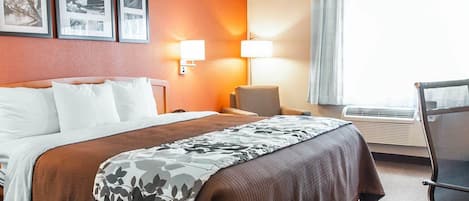 A hotel room with a large bed, a desk, a chair, and a window with curtains.