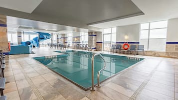 A large indoor swimming pool with a blue slide, seating area, and clear poolside views.