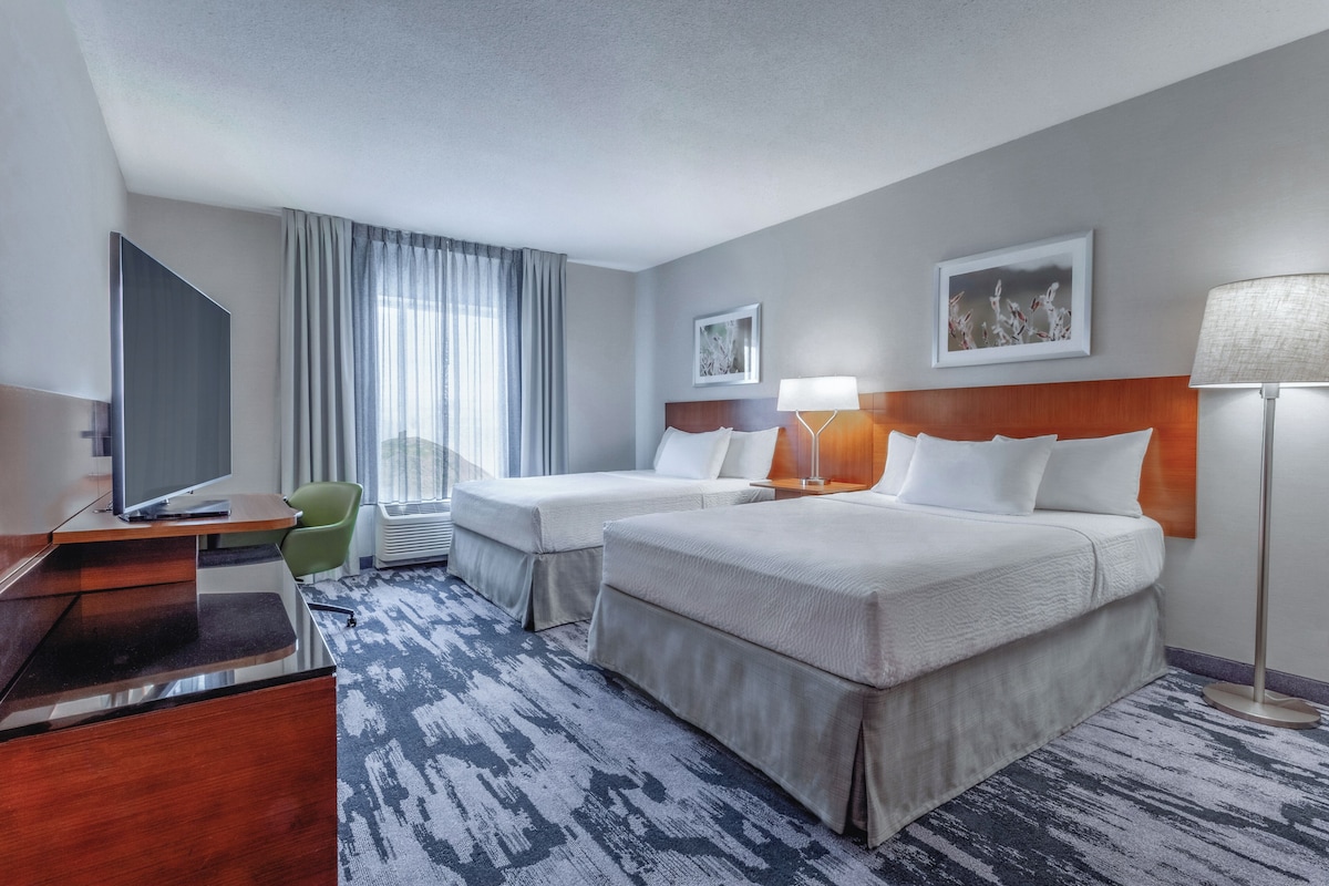 A hotel room with two beds, a desk, a chair, a TV, and a window with curtains.