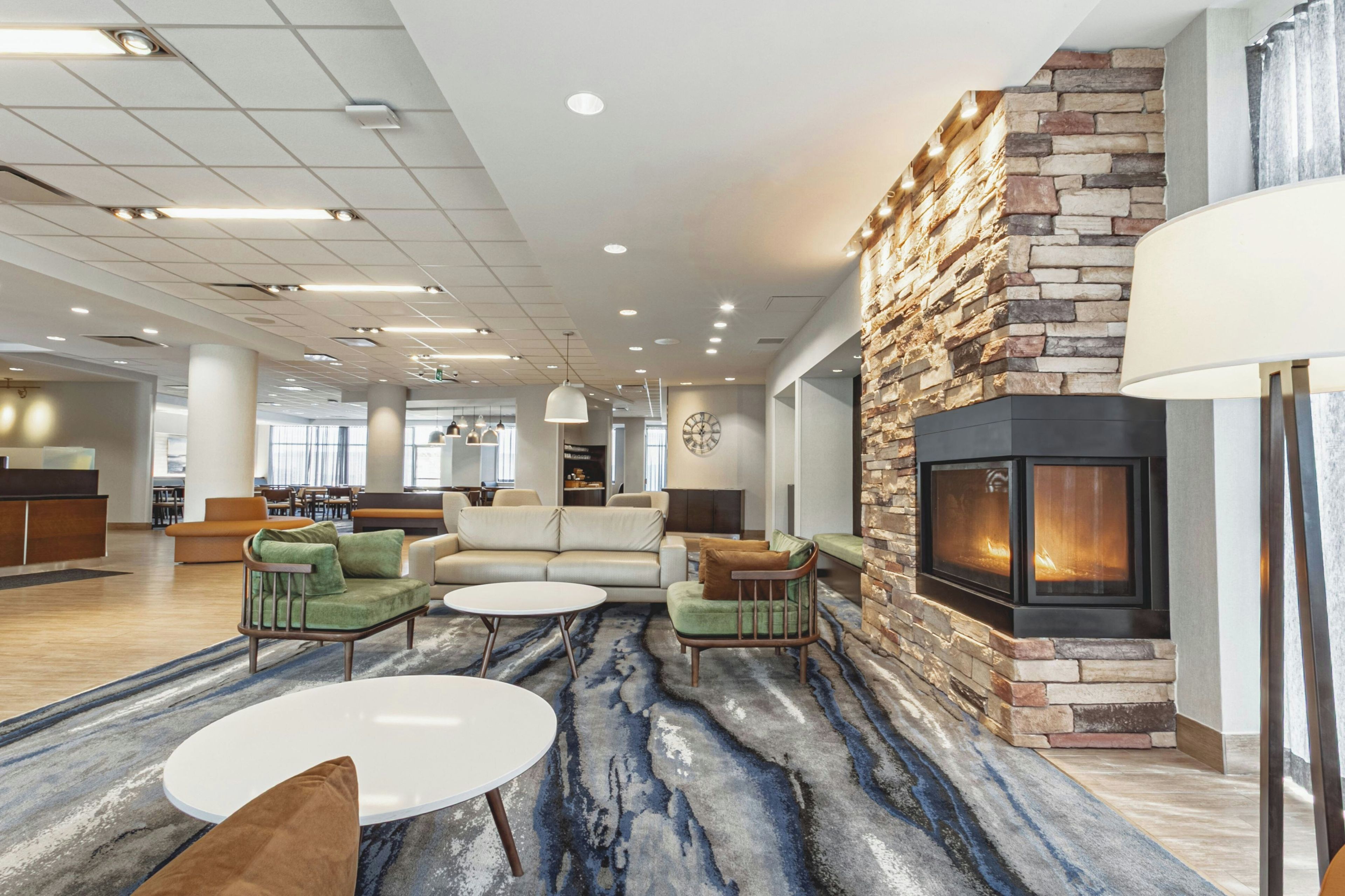 A spacious lobby with a stone fireplace, comfortable seating, and a modern ceiling design.