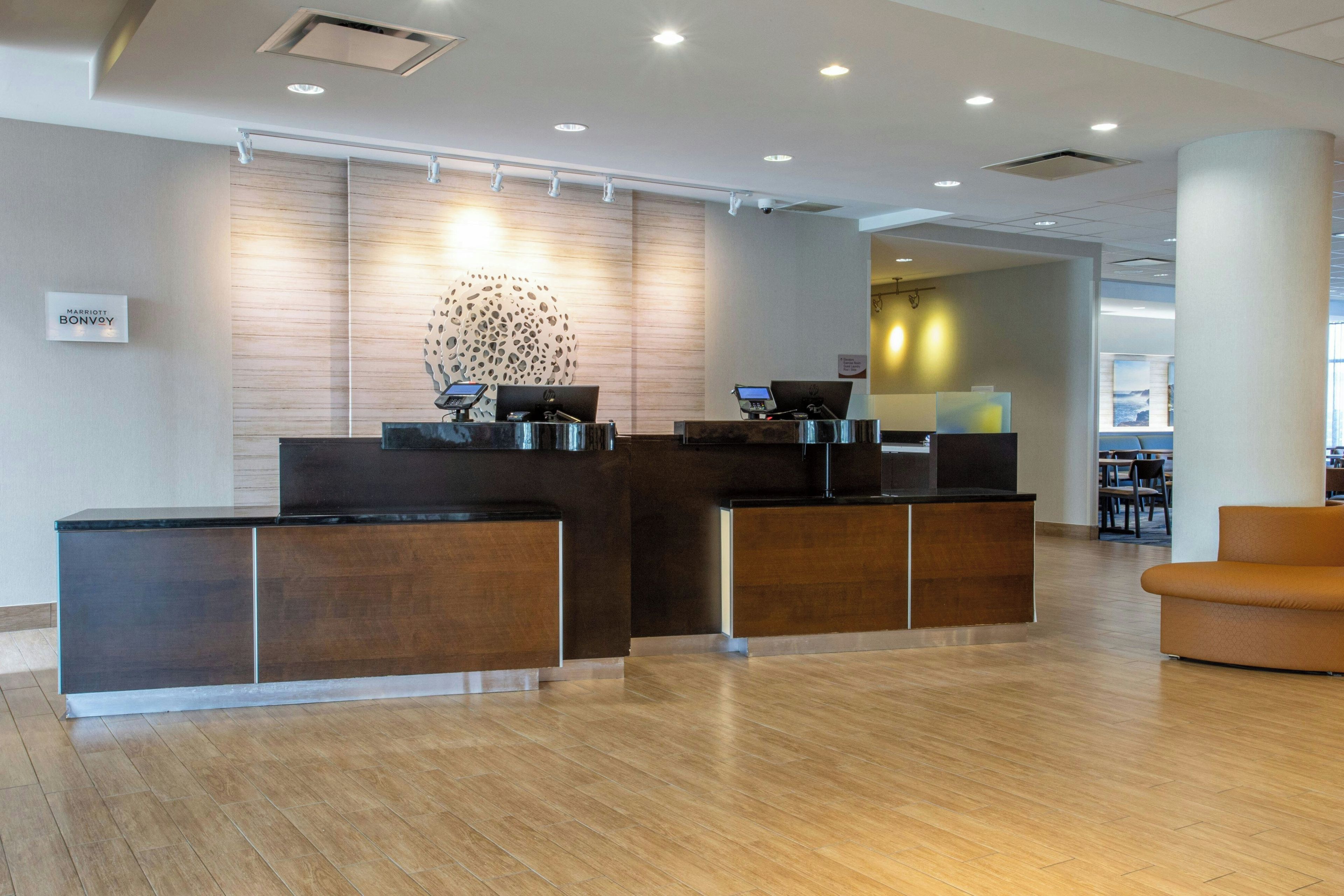 A hotel reception area with a wooden reception desk, a seating area, and a view of the lobby.