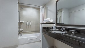 Un baño moderno con cabina de ducha, bañera, tocador con espejo grande y encimera con lavabo y grifo.