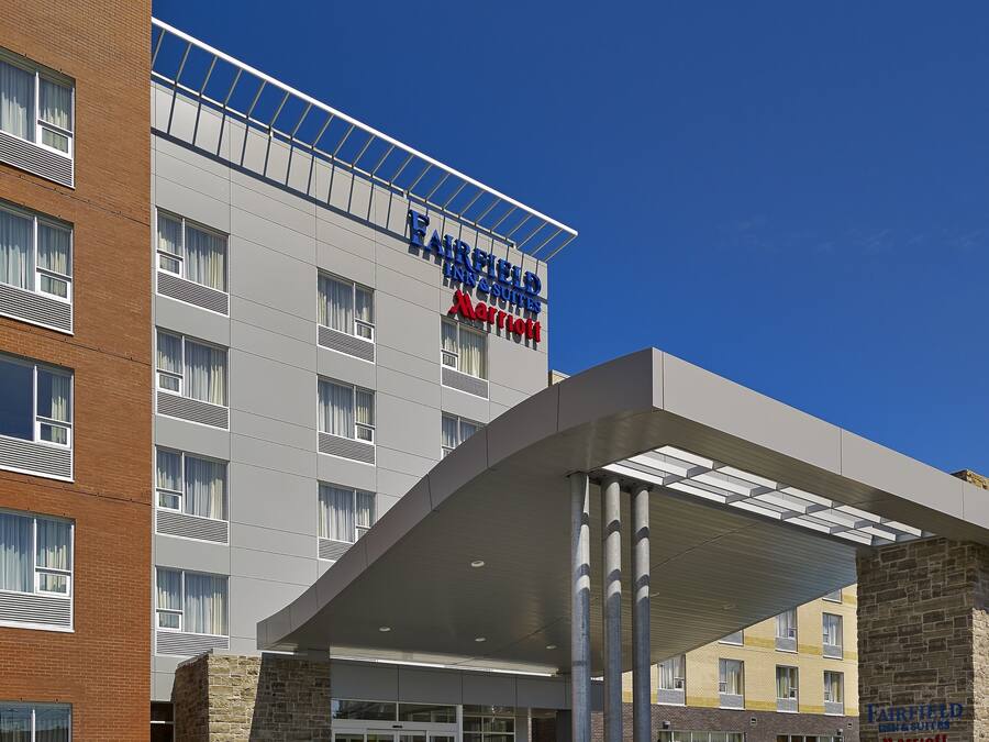 A Fairfield Inn & Suites by Marriott hotel with a modern design, featuring a prominent entrance and a clear blue sky.