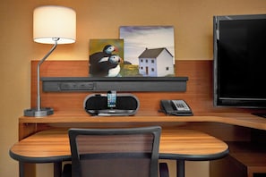 Une chambre d’hôtel avec un bureau en bois, une lampe, un tableau représentant des macareux et une maison, une télévision et un téléphone.