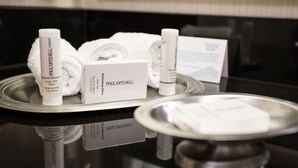 Artículos de tocador en una bandeja, incluyendo una botella de champú Paul Mitchell, toallas y una caja.