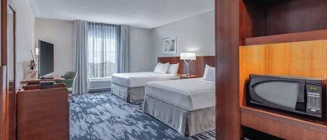 A hotel room with two beds, a desk, a chair, a television, a microwave, and a window with curtains.