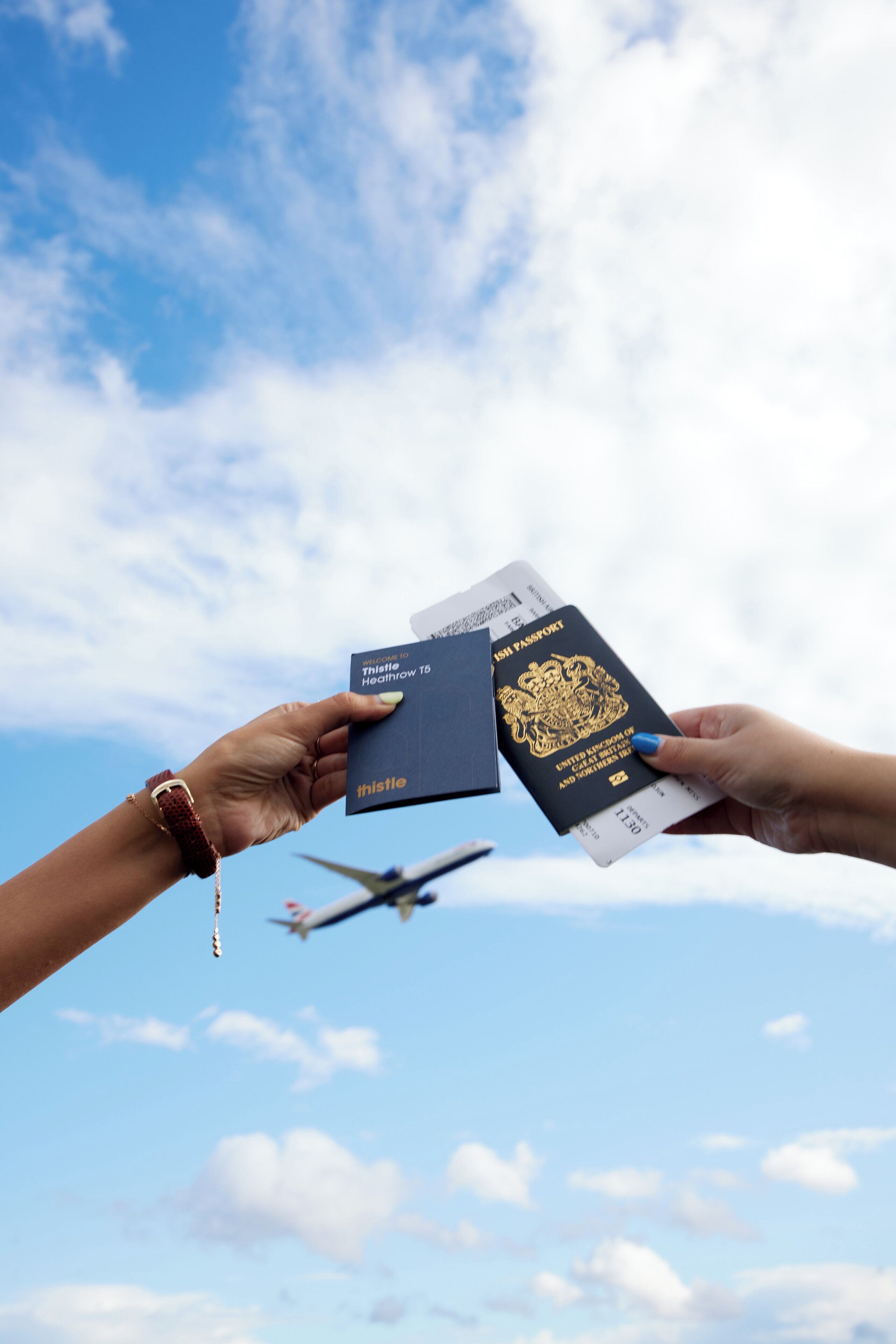 Una mà sosté un passaport i una targeta d'embarcament al fons d'un cel blau clar i un avió.