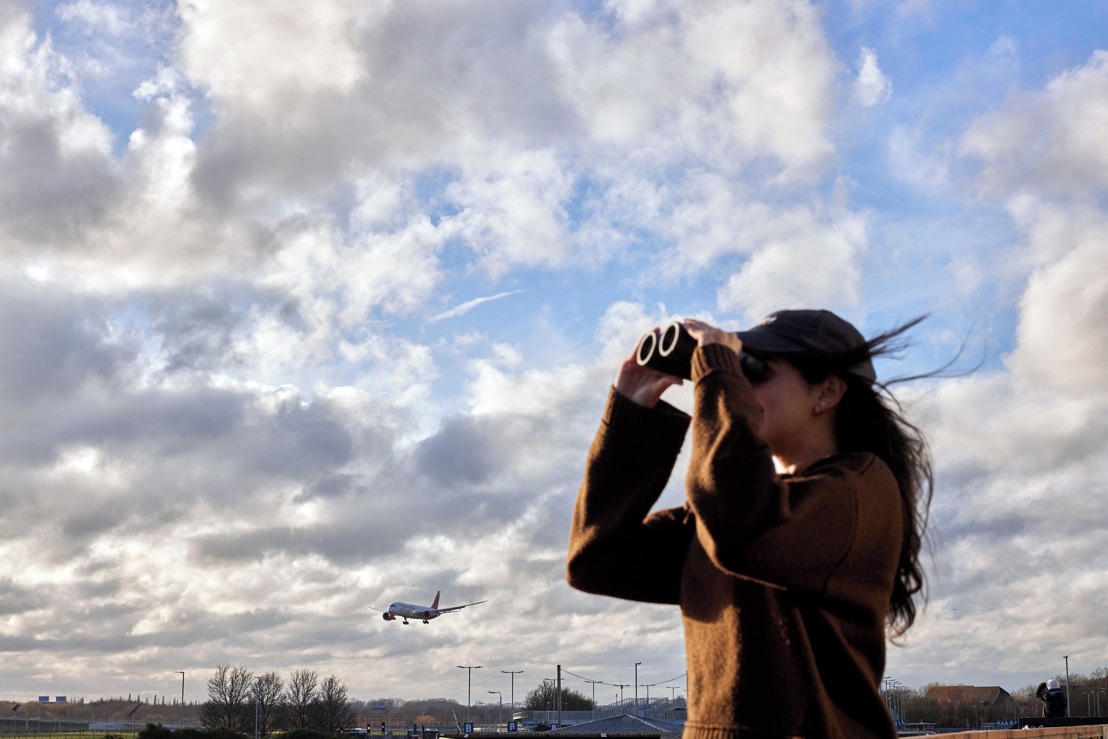 A person using binoculars to observe an airplane in the distance.