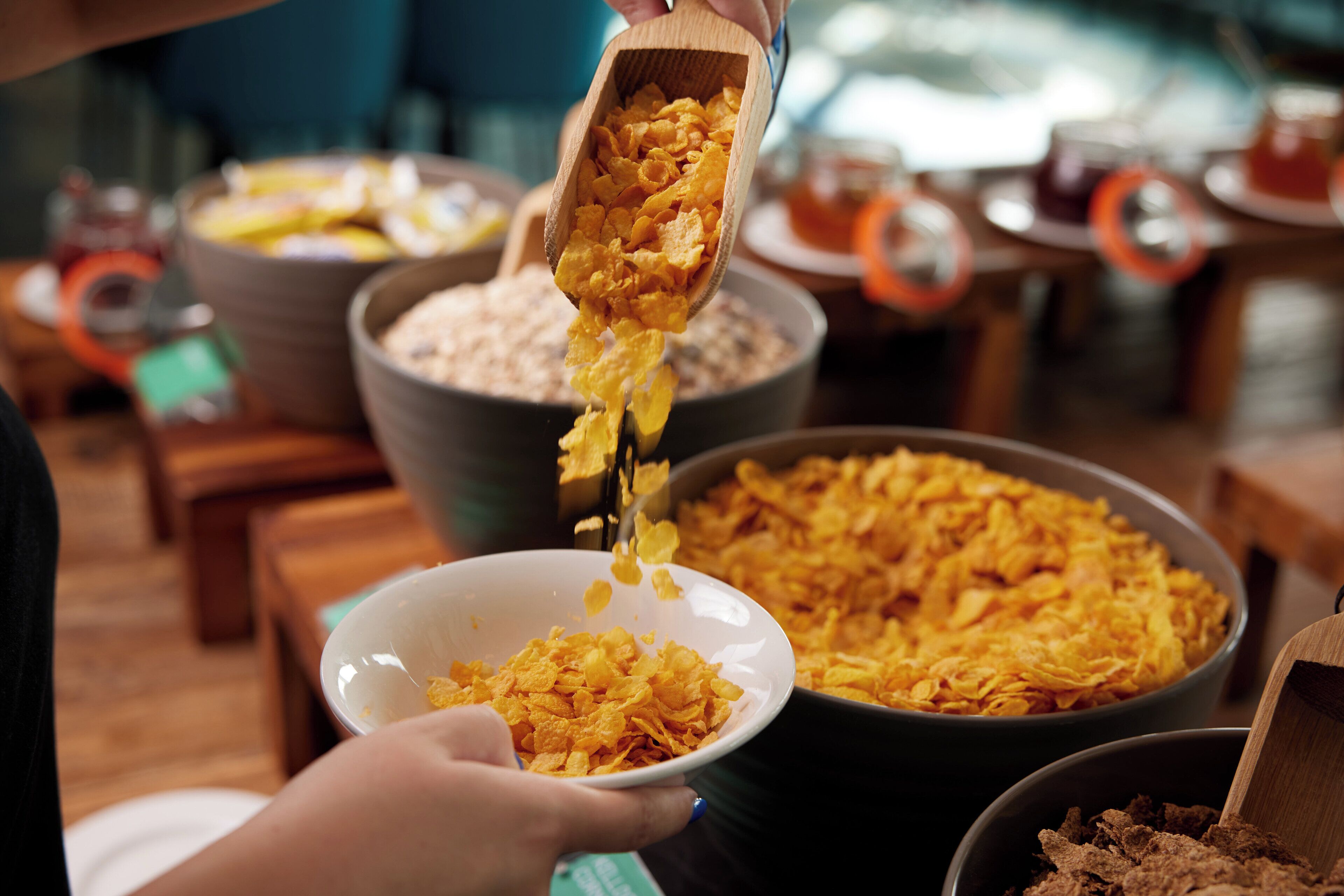 A person scooping cereal from a large bowl into a smaller bowl.