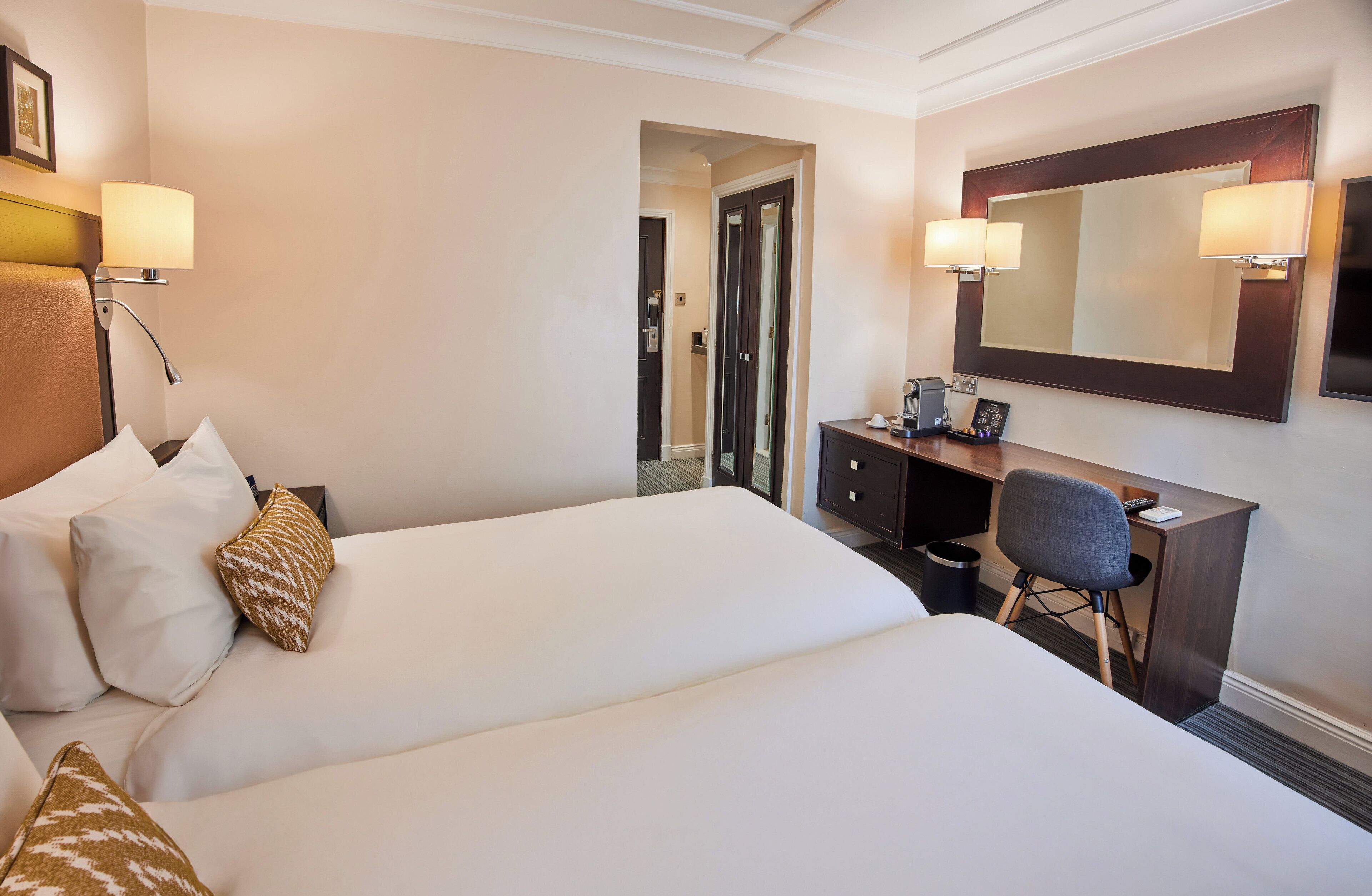 Een hotelkamer met twee bedden, een bureau, een stoel, een spiegel en een lamp.