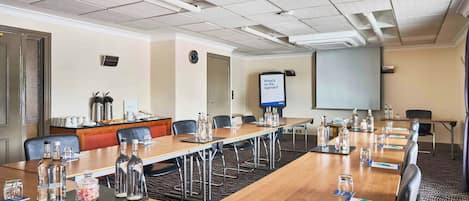 A conference room with a long table, chairs, a projector screen, and a coffee station.