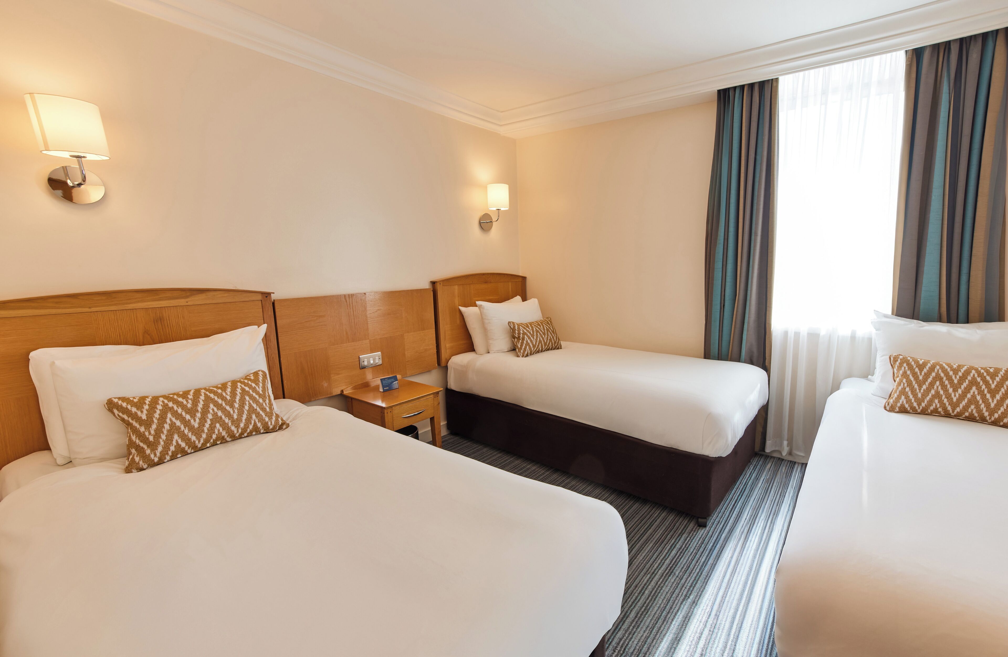 Een hotelkamer met twee bedden, een nachtkastje en een raam met gordijnen.