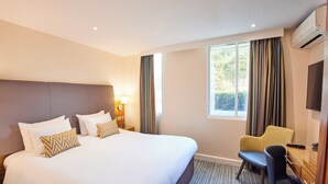 Una habitación de hotel con una cama grande, un escritorio con una silla, un televisor y una ventana con cortinas.