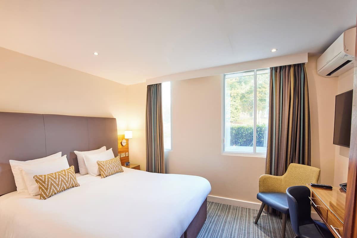 A hotel room with a large bed, a desk with a chair, a television, and a window with curtains.