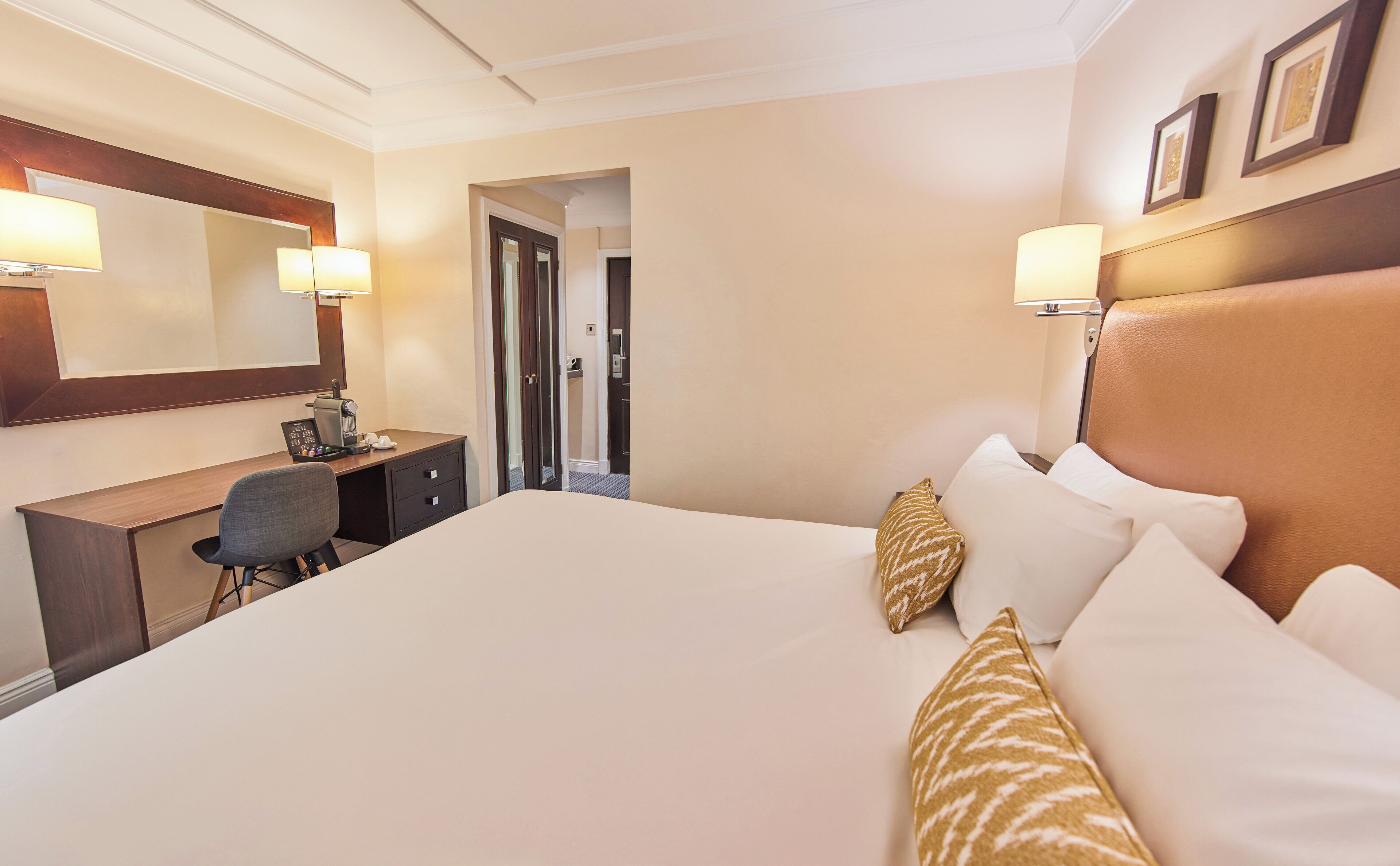 A hotel room with a large bed, a desk with a computer, and a mirror.