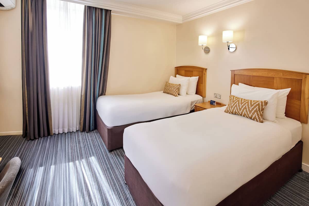 A hotel room with two beds, a desk, and a chair.