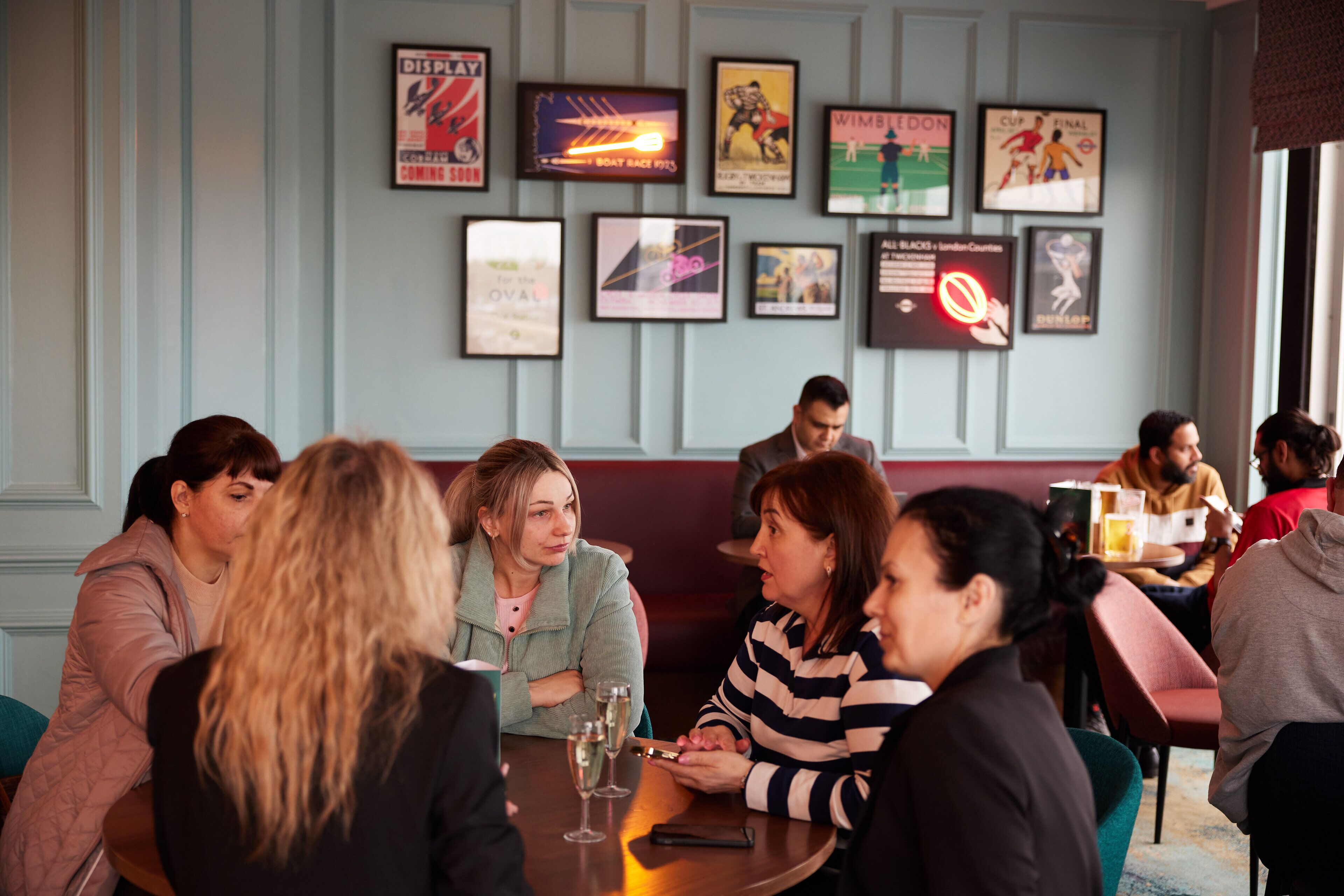 Un groupe de personnes est assis autour d’une table ronde dans un restaurant. Les murs sont décorés de cadres contenant des objets de collection liés au sport.