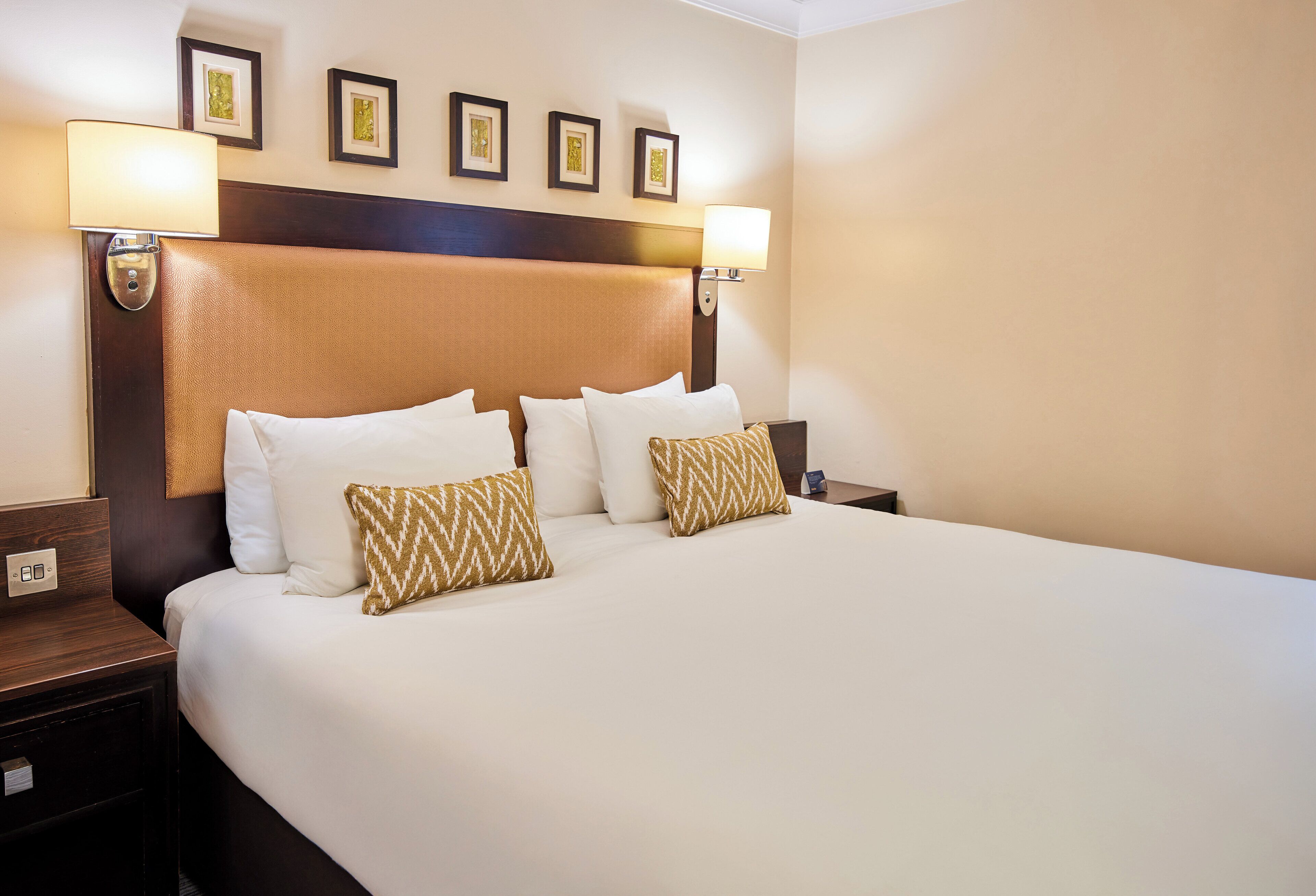 Una habitación de hotel con una cama grande, dos lámparas fijadas a la pared y obras de arte enmarcadas sobre la cama.