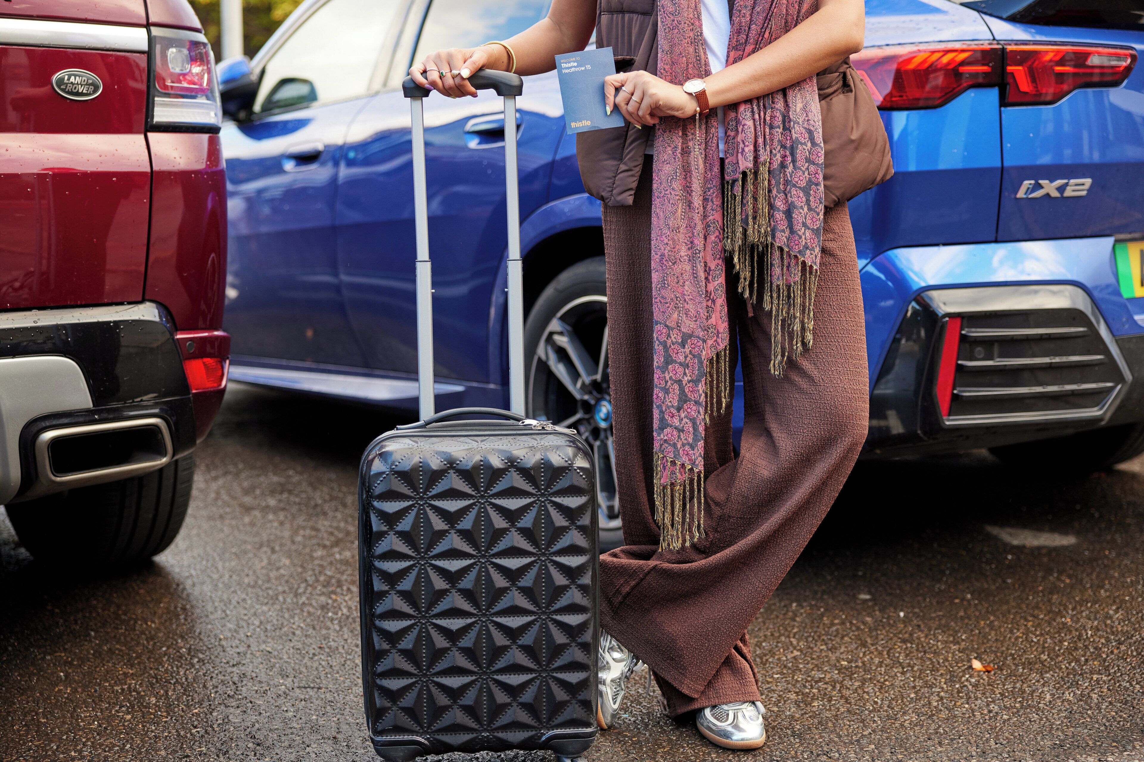 A person with a suitcase standing next to a blue car.