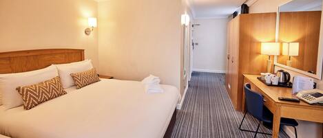A hotel room with a large bed, a desk with a lamp, and a mirror.