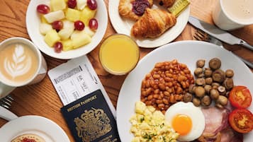 A breakfast table with a passport, a croissant, a plate of beans, mushrooms, tomatoes, and a plate of scrambled eggs and bacon.