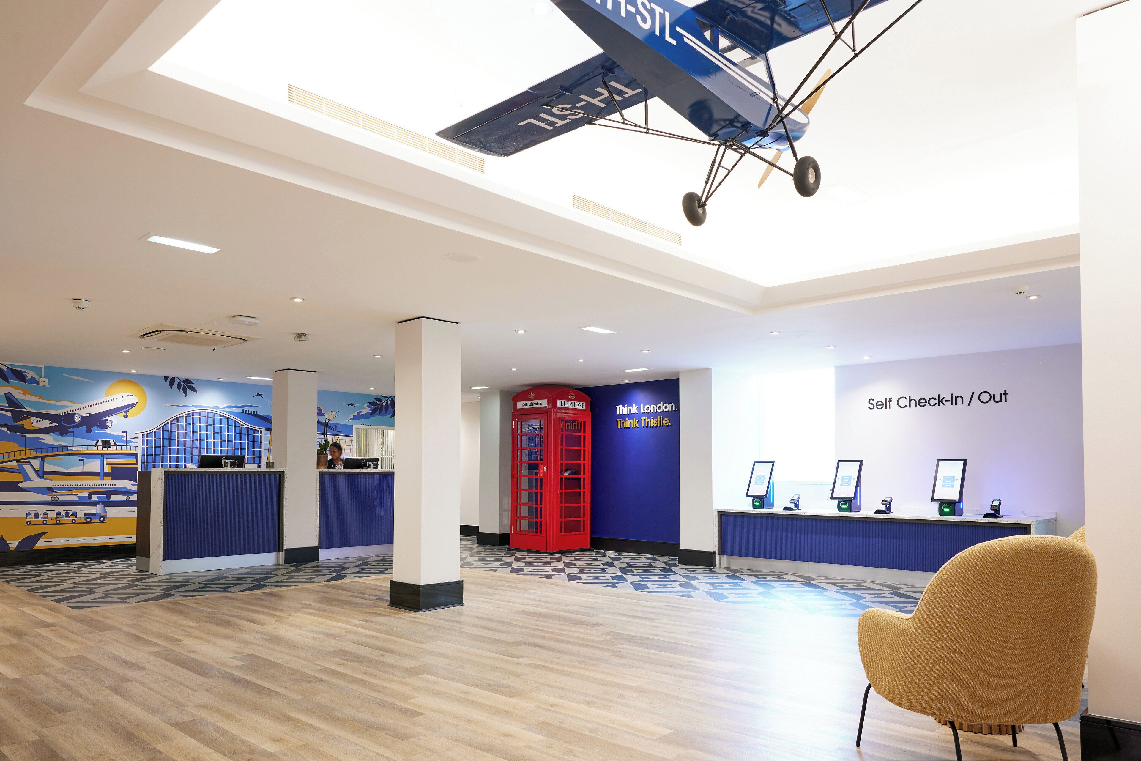 A modern reception area with a check-in/out station, a red telephone booth, and a large mural of an airplane.