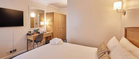 Habitación de hotel con cama, escritorio, silla, televisor de pantalla plana, espejo y lámpara de pared.